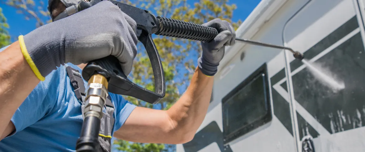 Worker pressure washing the exterior side of an RV to remove dirt and grime.