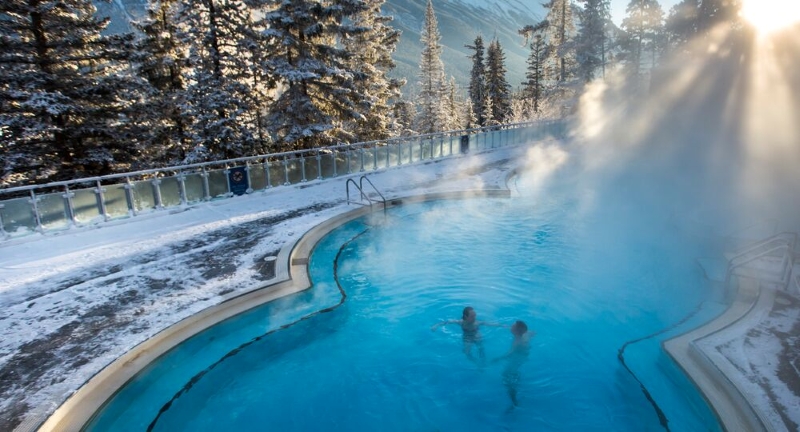 Soakers relax in a mountain-view hot spring pool with snow-covered peaks and clear blue skies in the background. Soakers relax in a mountain-view hot spring pool with snow-covered peaks and clear blue skies in the background.