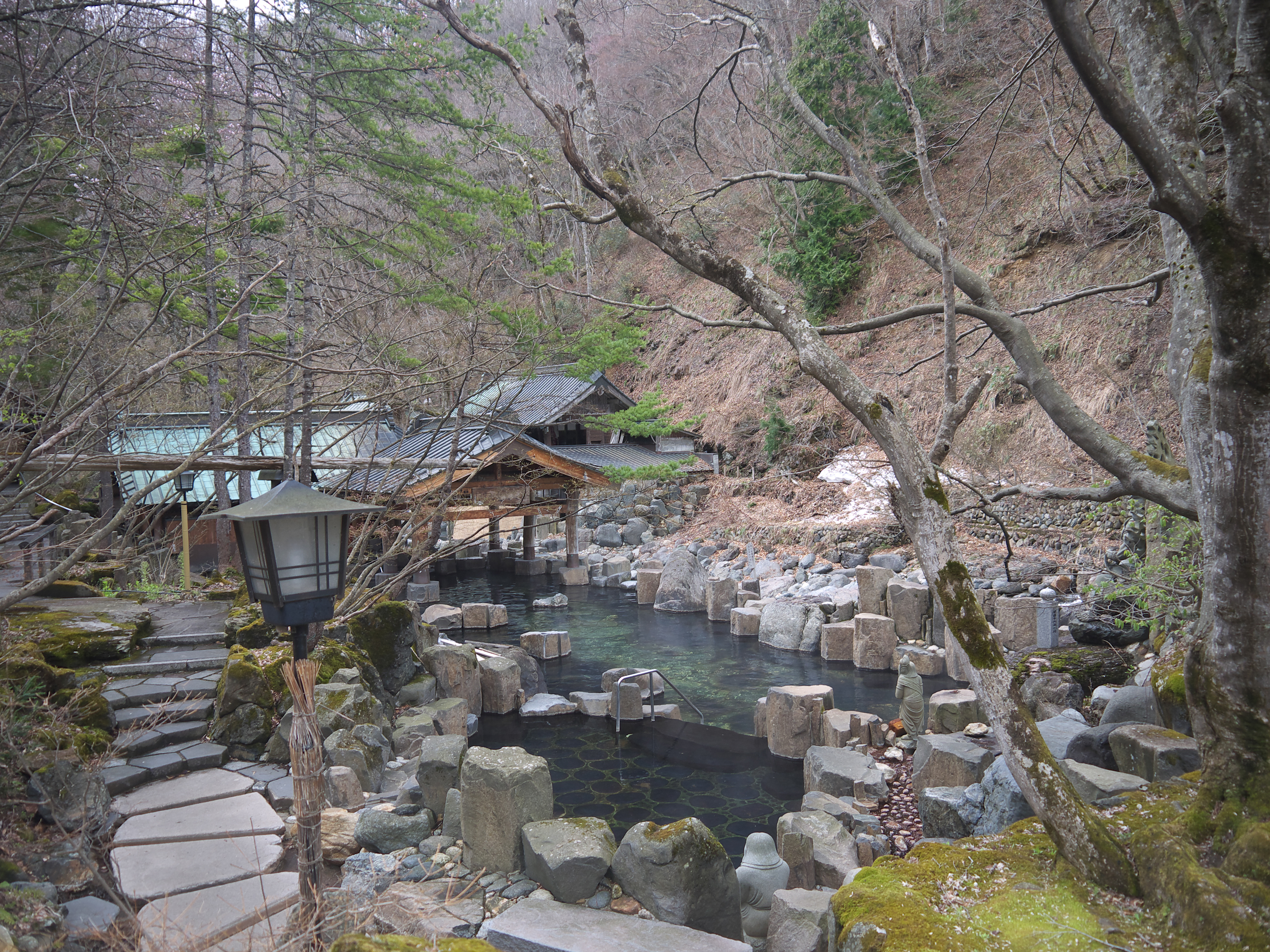 Large outdoor hot spring bath bordered by rocks and snow-covered trees beside a rushing river in Gunma Prefecture. Large outdoor hot spring bath bordered by rocks and snow-covered trees beside a rushing river in Gunma Prefecture.