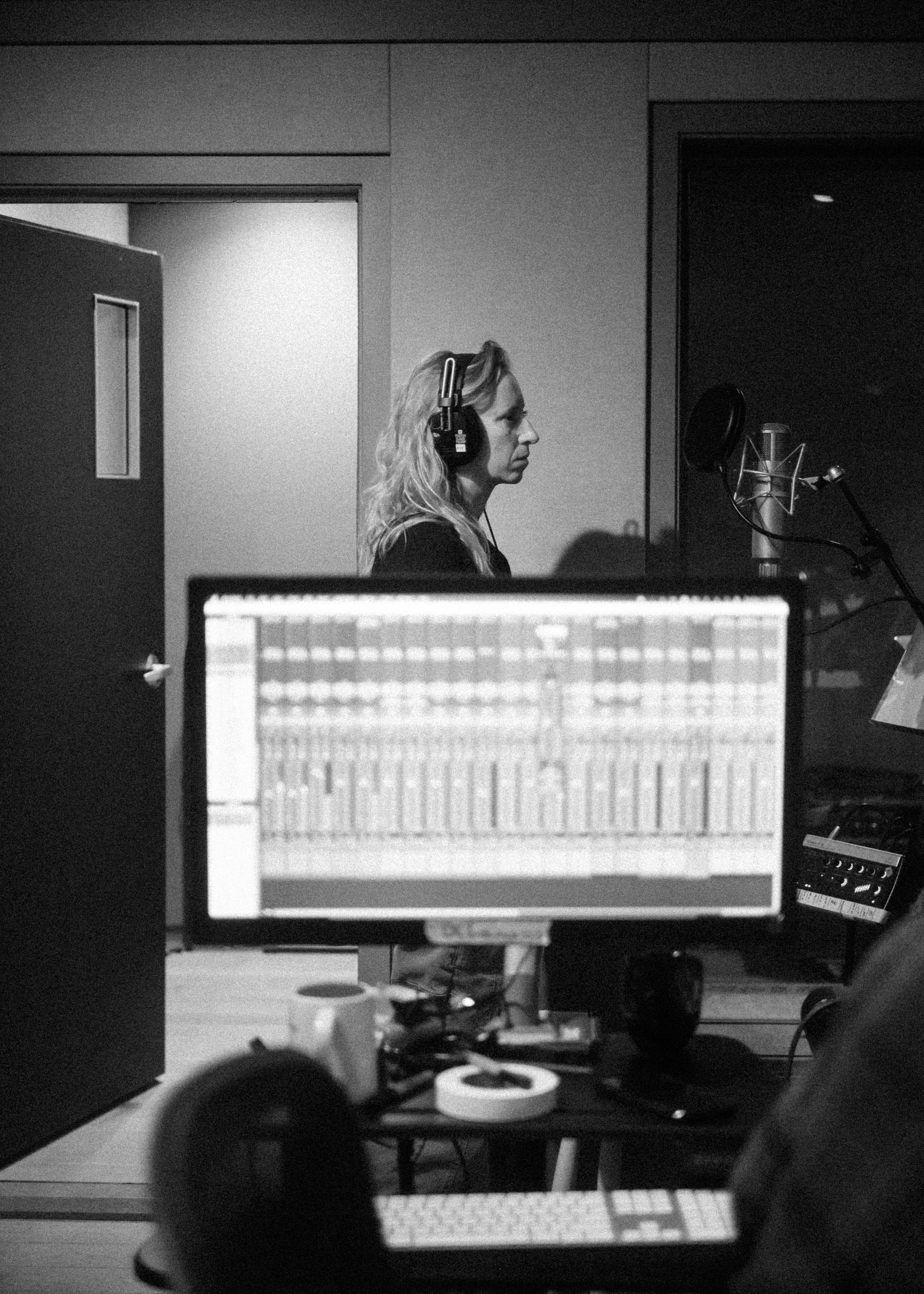 Jamie Wyman singing in the studio, wearing headphones, with view of control screen in the foreground
