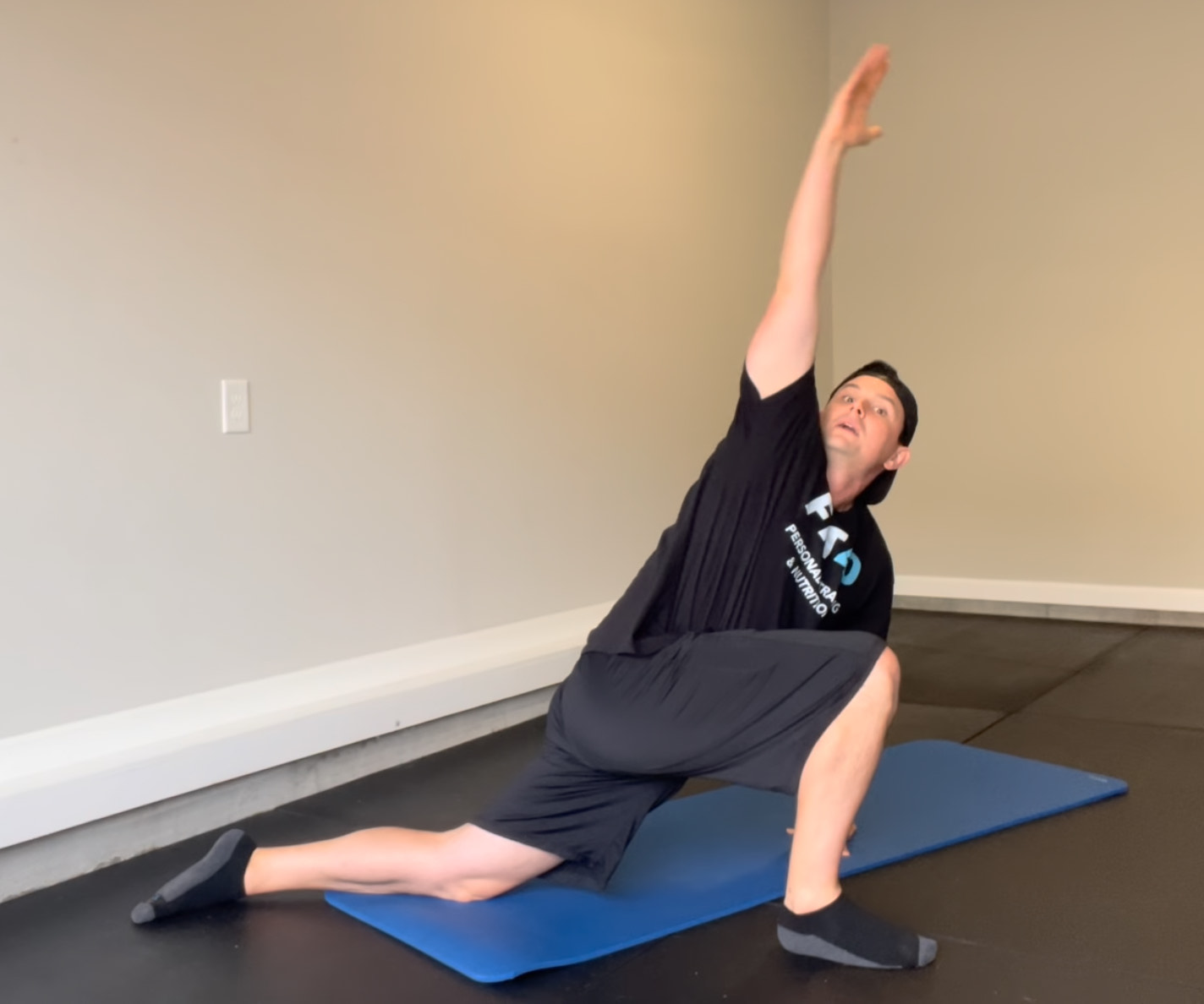 Bryan from FIT40 demonstrating the World’s Greatest Stretch on a gym mat, reaching one arm upward to improve hip, spine, and shoulder mobility for adults over 40.