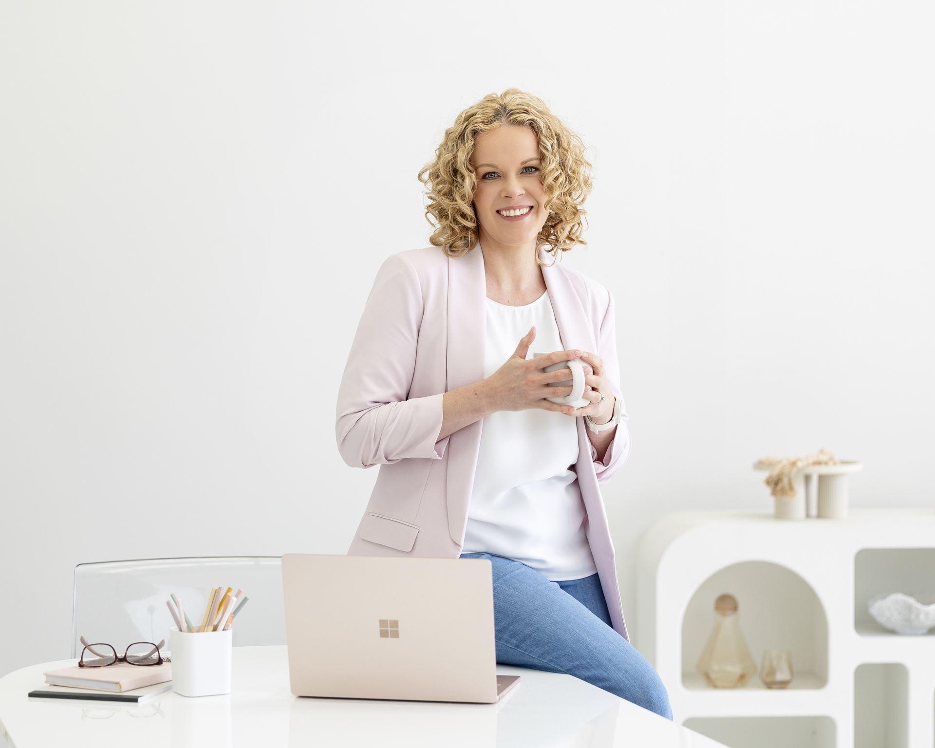 Personal branding image of a lady holding a cop of coffee and leaning on her desk in her office