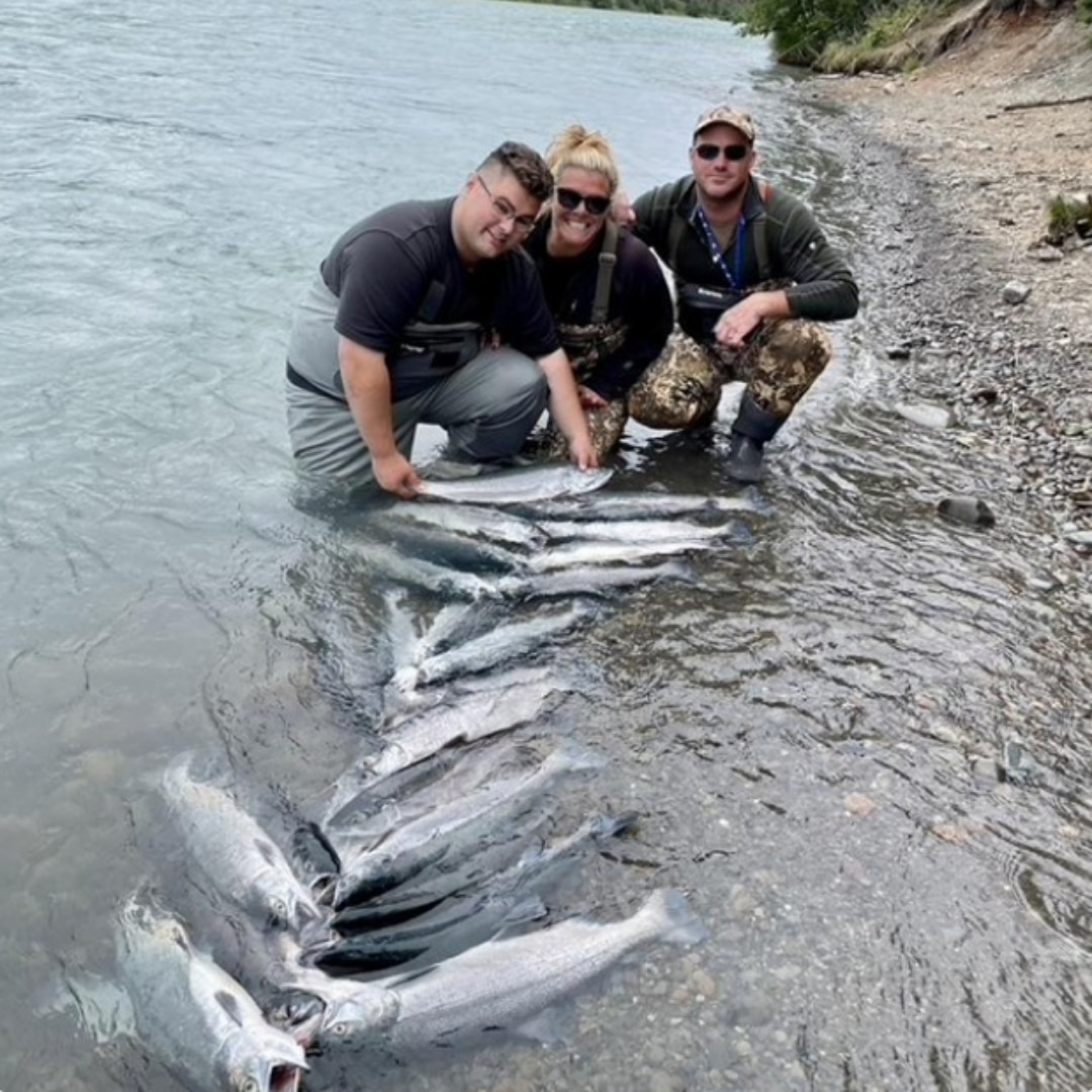 Dr. Barbara and two men in waders standing in a river with a large catch of salmon laid out in the shallow water.
