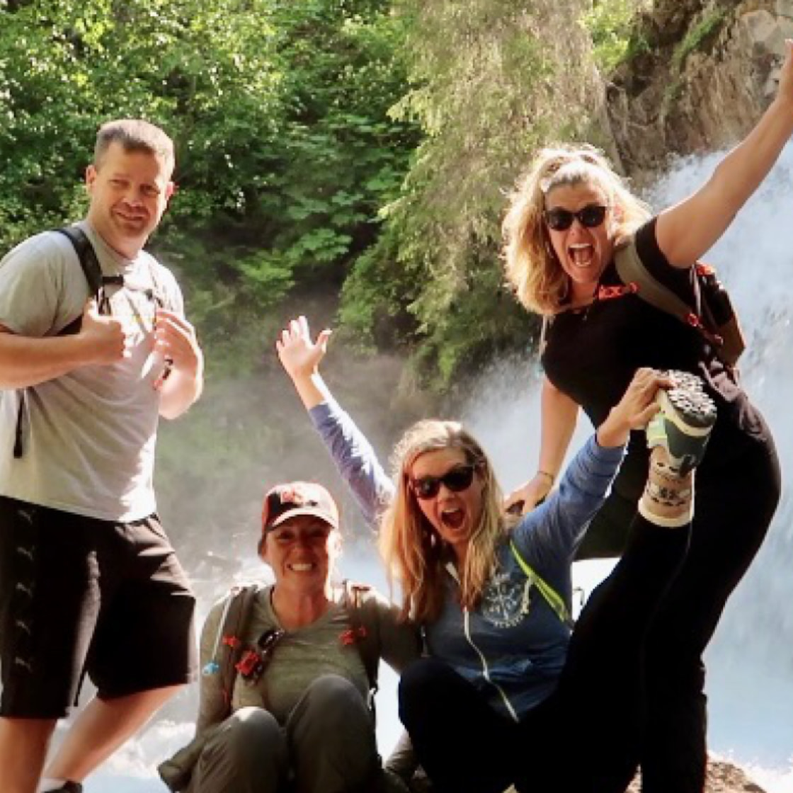 Dr. Barbara and three companions smiling and posing enthusiastically in front of a cascading waterfall amidst lush greenery.