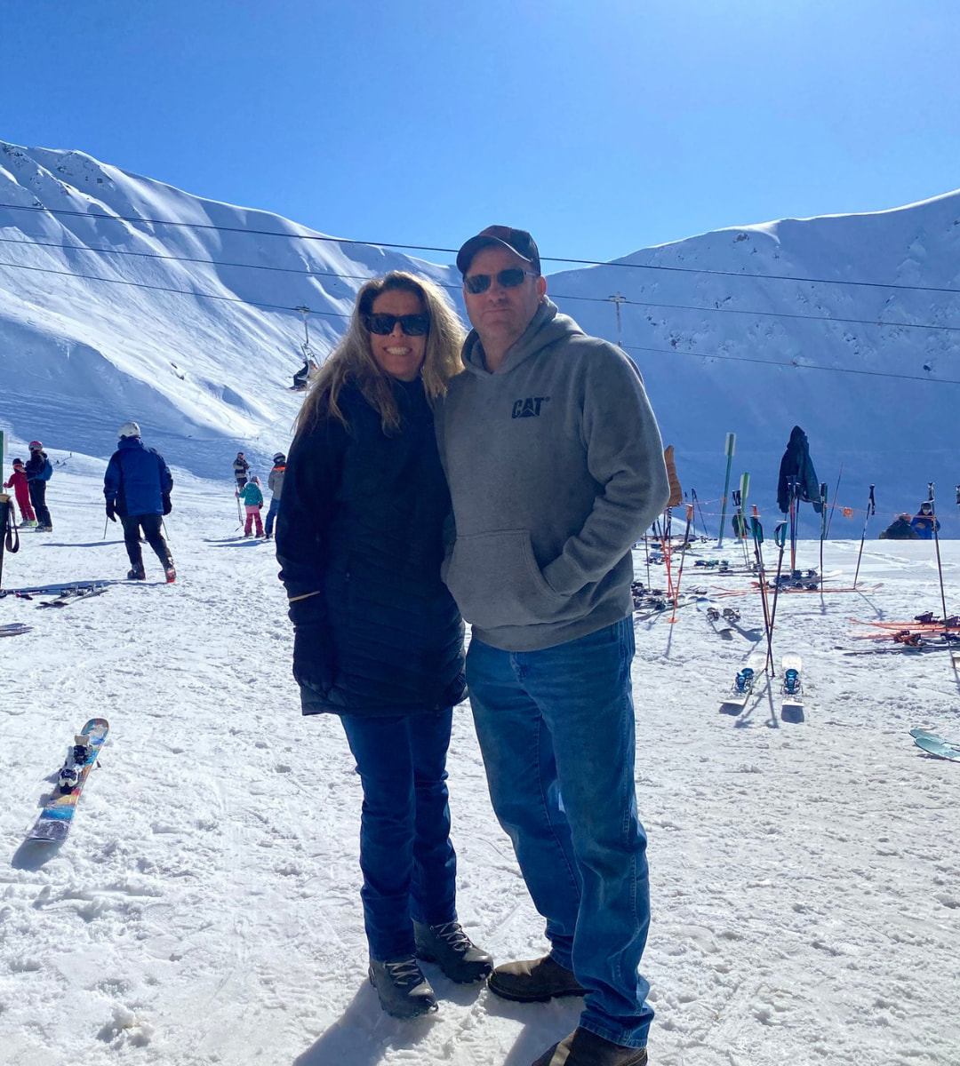 Dr. Barbara and another woman smiling and hugging on a snow-covered mountain peak, dressed in winter hiking gear.