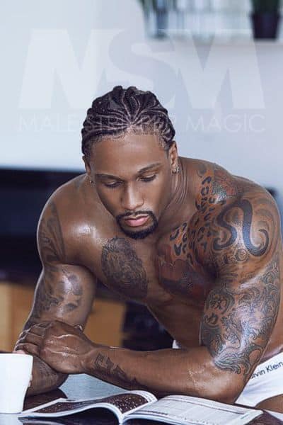 Black male stripper Pleasure with cornrows and tattoos reading a book