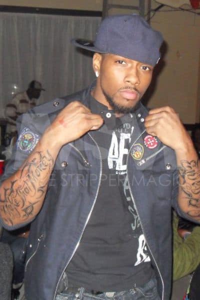 Black male stripper Pressure wearing navy blue fitted hat backwards, tattoos on arms