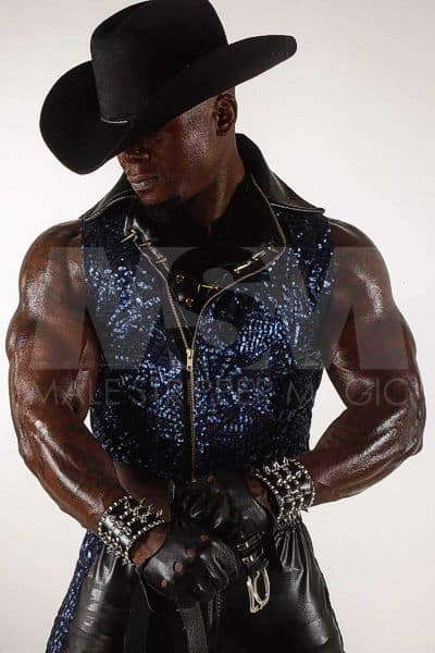 Black male stripper Incredible wearing black cowboy hat, sleeveless vest, leather gloves and pants, muscular