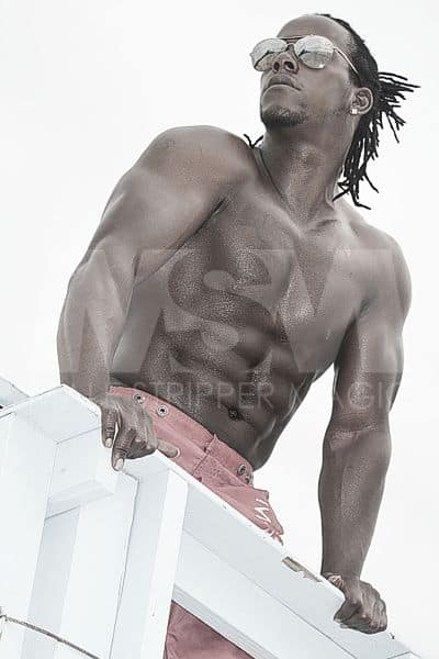 Black male stripper Kingston with dreads and sunglasses, no shirt on beach in lifeguard tower