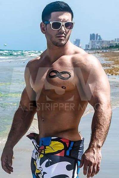 Male stripper Dominic on beach, muscular, sunglasses, wearing swim trunks