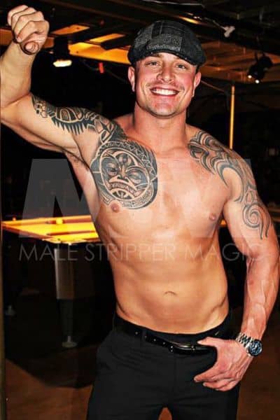 Male stripper Dean wearing newsboy hat and no shirt, tattoos, black pants and a watch in nightclub