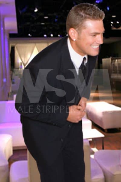 Male stripper RJ, smiling, wearing a suit at a fancy male revue club