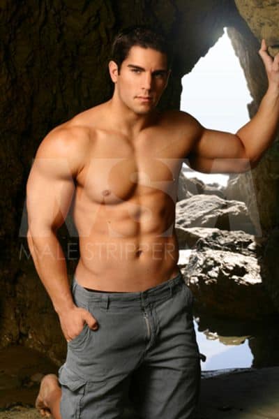 Male stripper Ethan on beach rocks, shirtless, wearing cargo shorts
