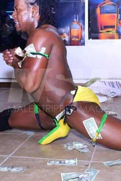 Black male stripper Kingston performing at a male revue, green and yellow Jamaican style, dollars everywhere, and sweaty