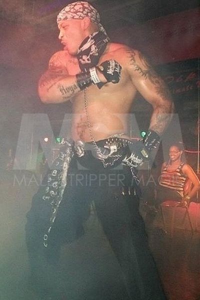 Black male stripper Temptation, shirtless, performing on stage at a nightclub wearing bandanas and gloves