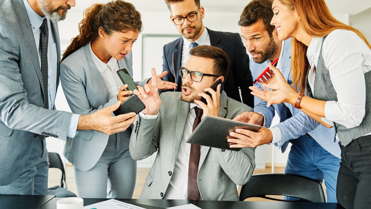 Overwhelmed business executive surrounded by coworkers seeking help, symbolizing the stress of unmanaged cybersecurity risks Overwhelmed business executive surrounded by coworkers seeking help, symbolizing the stress of unmanaged cybersecurity risks