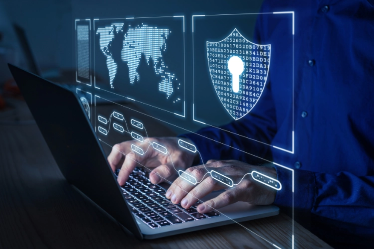 Man typing on laptop with digital security interface showing shield, world map, and data flows, symbolizing layered cybersecurity defense Man typing on laptop with digital security interface showing shield, world map, and data flows, symbolizing layered cybersecurity defense
