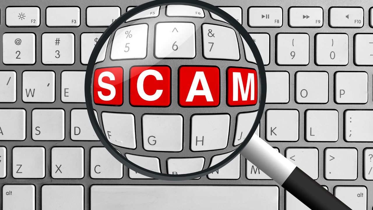 Magnifying glass highlighting the word SCAM on keyboard to illustrate digital SMS phishing and smishing scams Magnifying glass highlighting the word SCAM on keyboard to illustrate digital SMS phishing and smishing scams