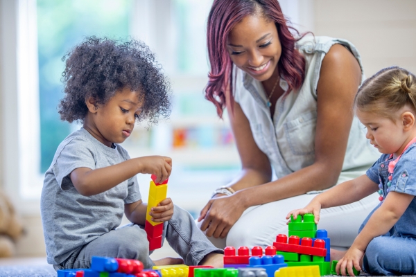 Child playing with colorful building blocks alongside a caregiver, promoting creativity and learning in a daycare setting. Child playing with colorful building blocks alongside a caregiver, promoting creativity and learning in a daycare setting.
