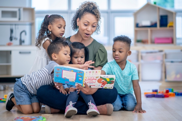 Caregiver reading a colorful book with four engaged children in a daycare setting, promoting early childhood education and nurturing interaction. Caregiver reading a colorful book with four engaged children in a daycare setting, promoting early childhood education and nurturing interaction.