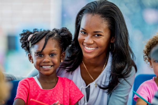 Smiling caregiver and child in a colorful learning environment, highlighting personalized attention in childcare settings. Smiling caregiver and child in a colorful learning environment, highlighting personalized attention in childcare settings.