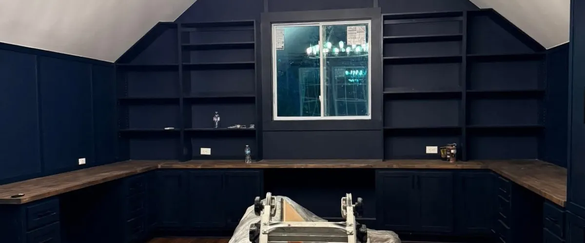 Home office setup with navy blue built-in shelves and wood countertops around a window Home office setup with navy blue built-in shelves and wood countertops around a window
