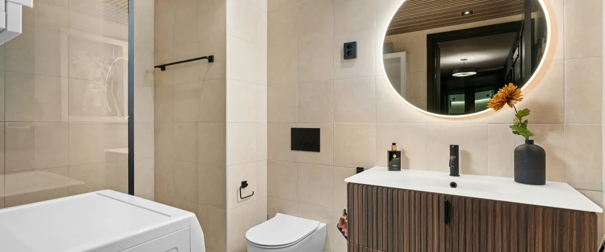 Minimalist bathroom with a floating vanity and circular backlit mirror above the sink Minimalist bathroom with a floating vanity and circular backlit mirror above the sink