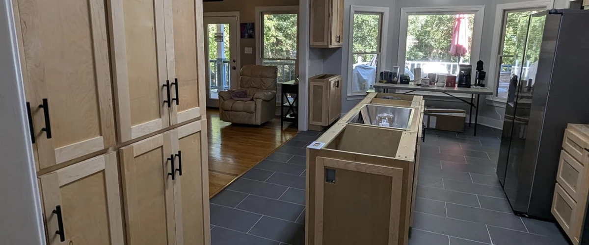 Modern kitchen layout featuring natural wood cabinets, large windows, and open space with gray tile flooring.