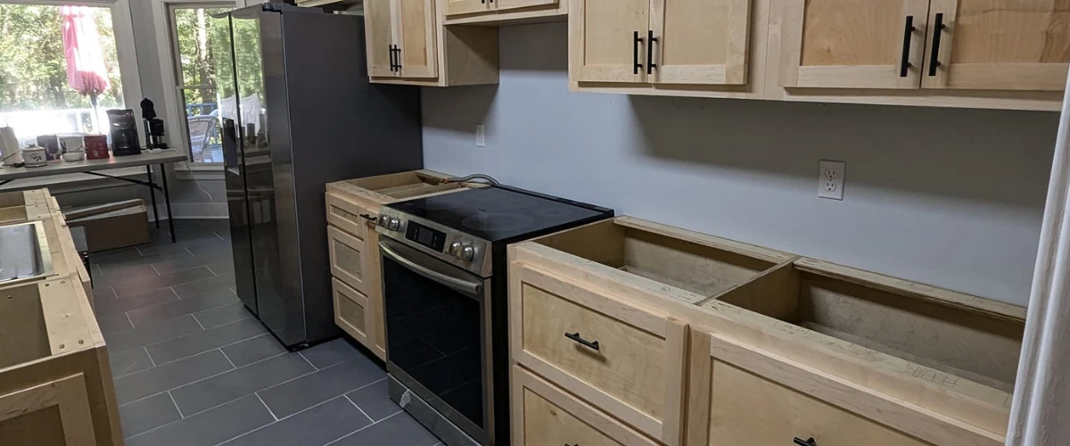 Kitchen renovation with new wood cabinets, oven, and stainless steel refrigerator under bright natural lighting.