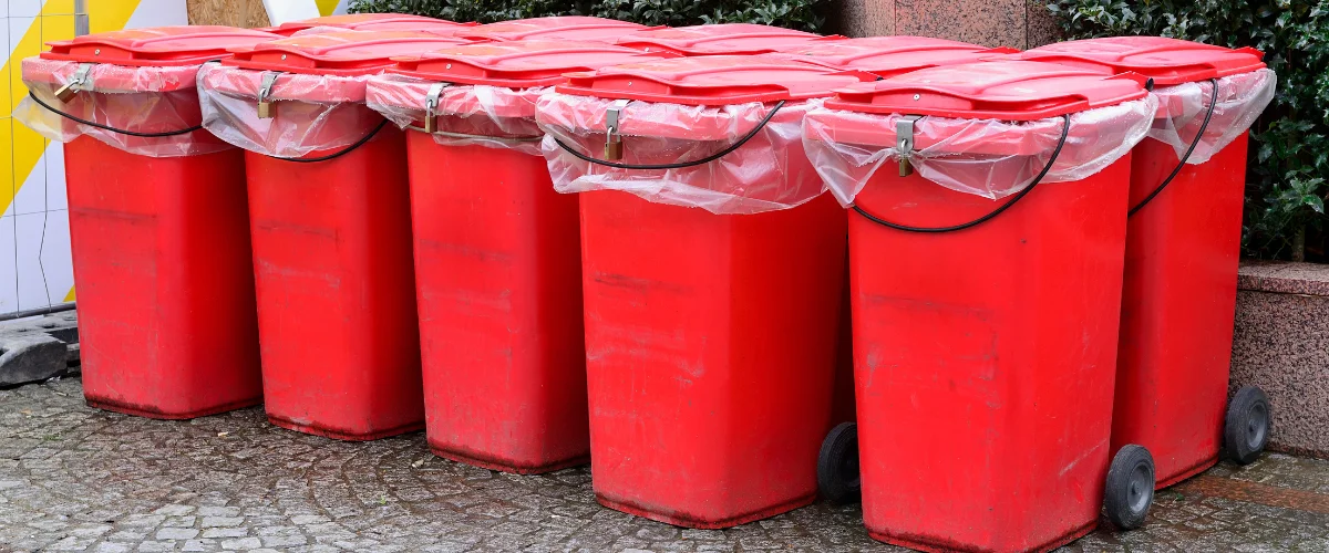 Row of red trash bins with plastic liners placed outdoors.