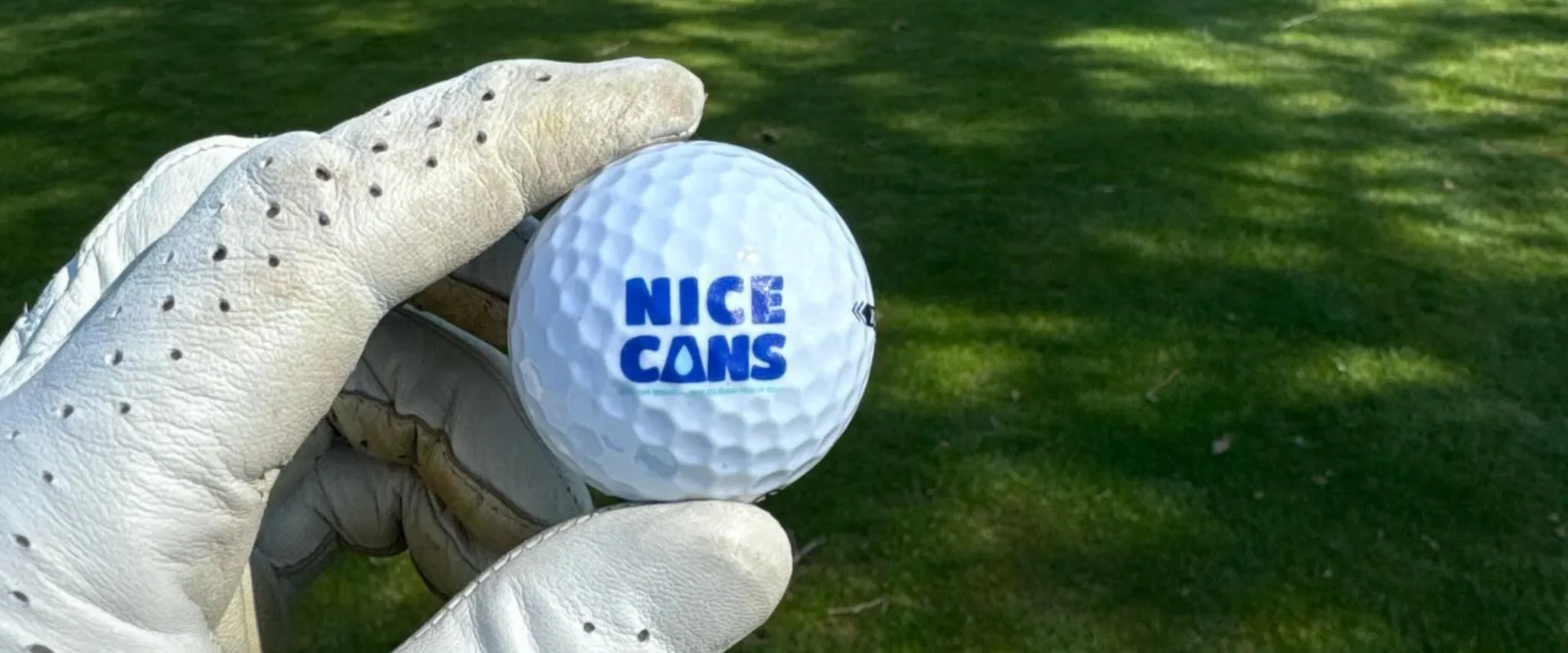 Golf ball with 'Nice Cans' branding held by a gloved hand on a green golf course Golf ball with 'Nice Cans' branding held by a gloved hand on a green golf course