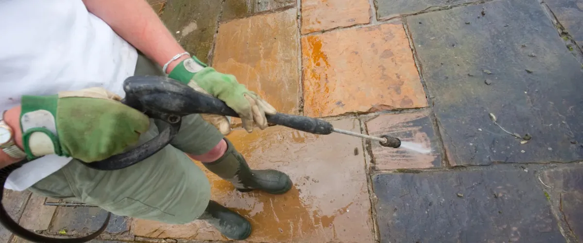 Person using a pressure washer to clean a stone patio, removing dirt and stains Person using a pressure washer to clean a stone patio, removing dirt and stains