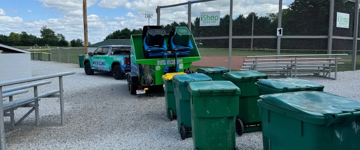 Professional trash bin cleaning station servicing multiple green garbage cans near a field."