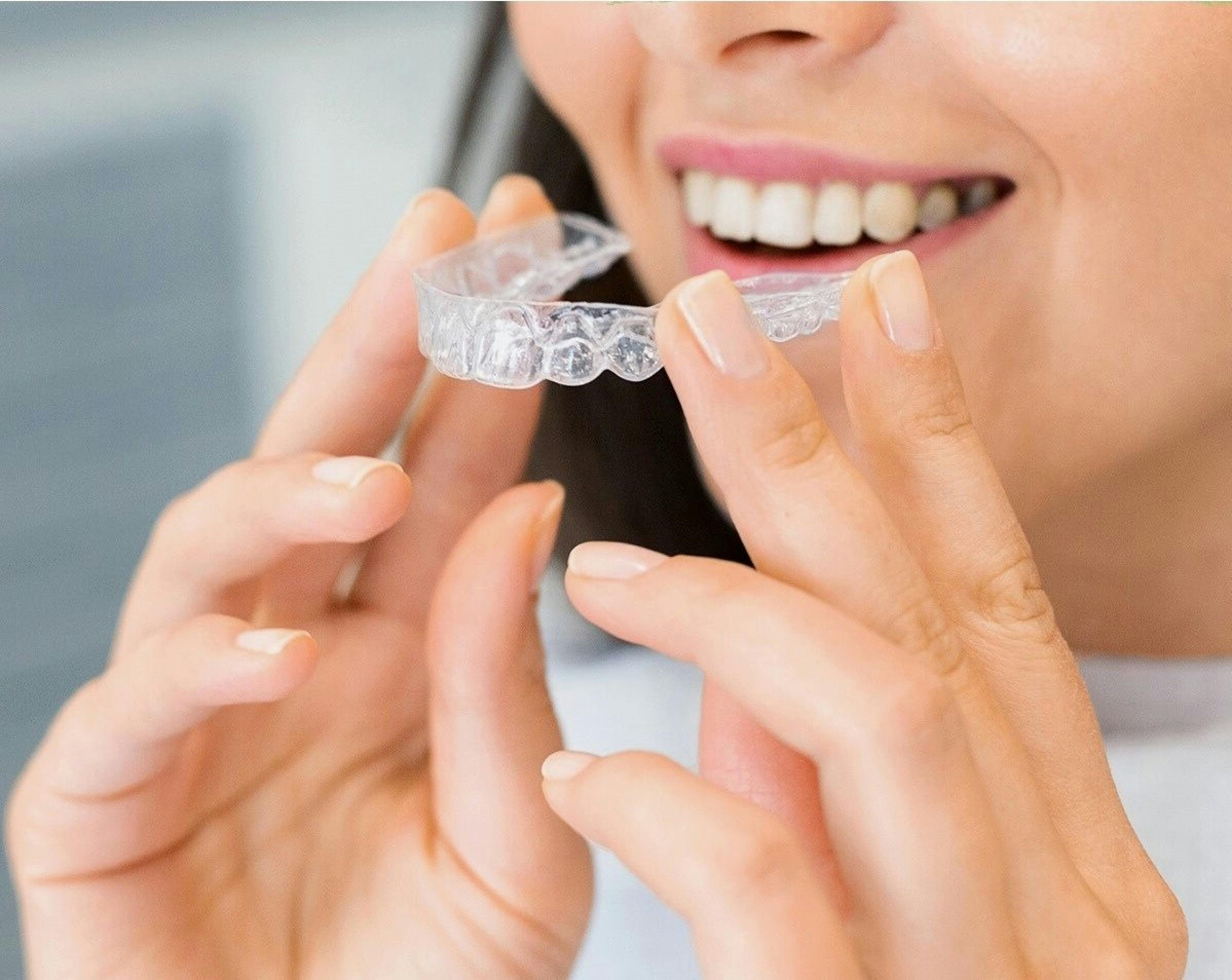 A woman holding up Invisalign in front of her perfect teeth A woman holding up Invisalign in front of her perfect teeth