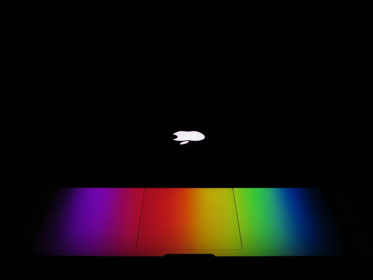 A laptop in a dark setting with its closed lid illuminated by a rainbow of colors, reflecting a vibrant spectrum on the surface beneath the glowing Apple logo. Every Task Virtual Assistants USA. A laptop in a dark setting with its closed lid illuminated by a rainbow of colors, reflecting a vibrant spectrum on the surface beneath the glowing Apple logo. Every Task Virtual Assistants USA.