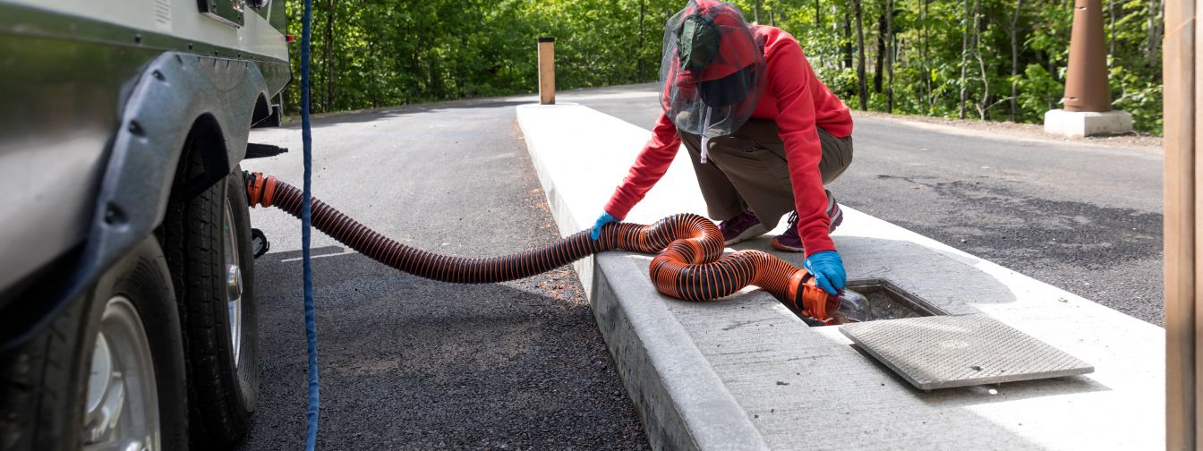 A worker in protective gear and gloves connecting a sewer hose to an RV dump station. Proper wastewater disposal and regular sewer maintenance help prevent backups and ensure sanitation in outdoor settings. A worker in protective gear and gloves connecting a sewer hose to an RV dump station. Proper wastewater disposal and regular sewer maintenance help prevent backups and ensure sanitation in outdoor settings.