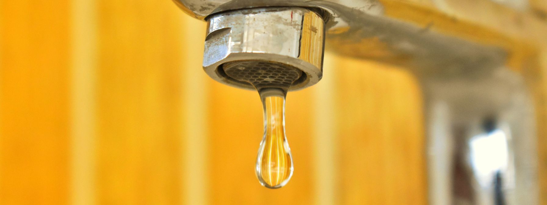 Close-up of a dripping faucet with a single droplet of water suspended—illustrating a common household leak that can lead to higher water bills if left unaddressed.
