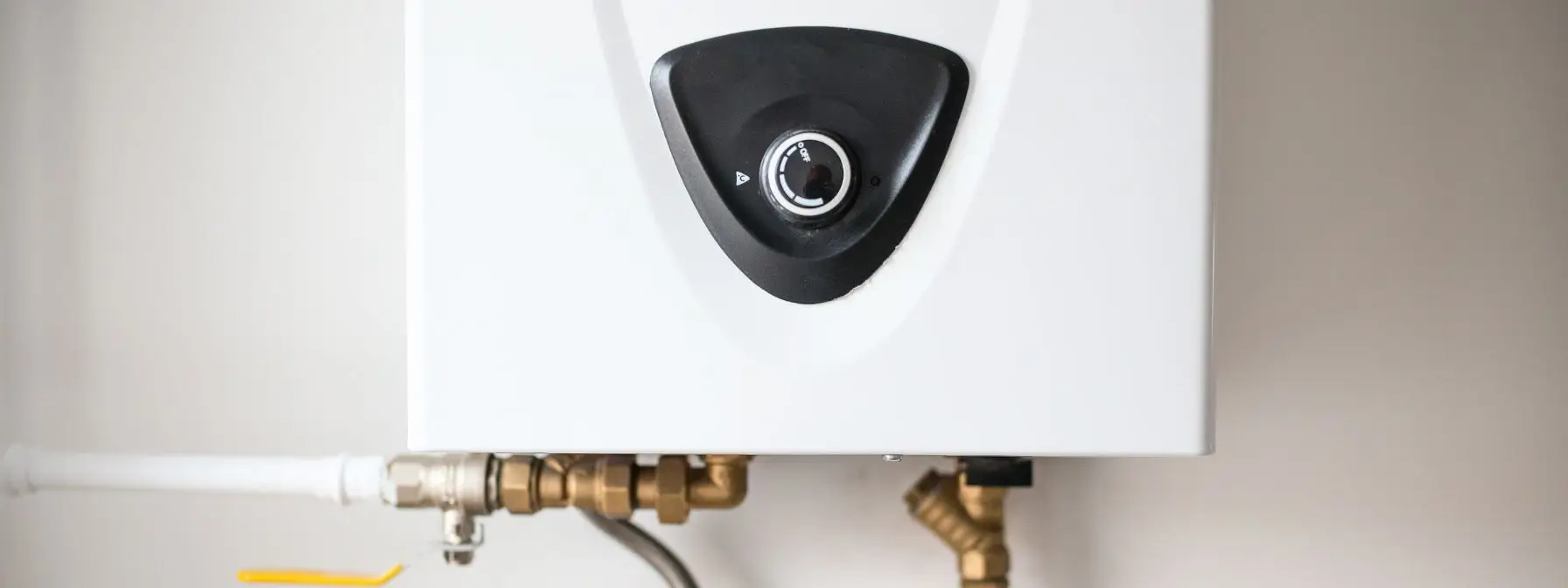Close-up view of a modern tankless water heater mounted on a wall, showing the temperature control dial and plumbing connections—highlighting common inspection points for wear or leaks.