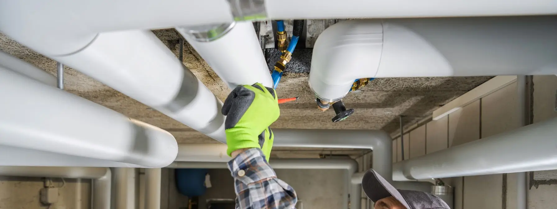 A plumber in a green glove inspects and adjusts insulated water pipes on a basement ceiling, illustrating the importance of regular maintenance to catch hidden plumbing issues before they escalate. A plumber in a green glove inspects and adjusts insulated water pipes on a basement ceiling, illustrating the importance of regular maintenance to catch hidden plumbing issues before they escalate.
