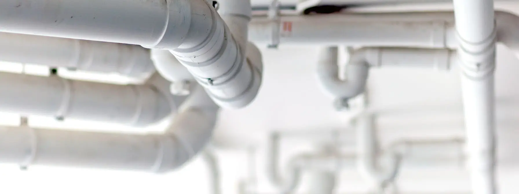 Close-up view of white PVC plumbing pipes running along a ceiling, emphasizing how hidden plumbing systems can conceal leaks or issues that lead to major damage if not inspected and maintained regularly. Close-up view of white PVC plumbing pipes running along a ceiling, emphasizing how hidden plumbing systems can conceal leaks or issues that lead to major damage if not inspected and maintained regularly.
