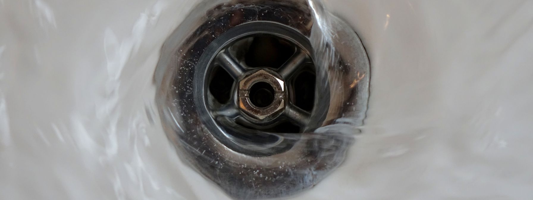 Close-up of water swirling down a sink drain, illustrating proper drainage and the importance of keeping pipes clear to prevent plumbing emergencies.