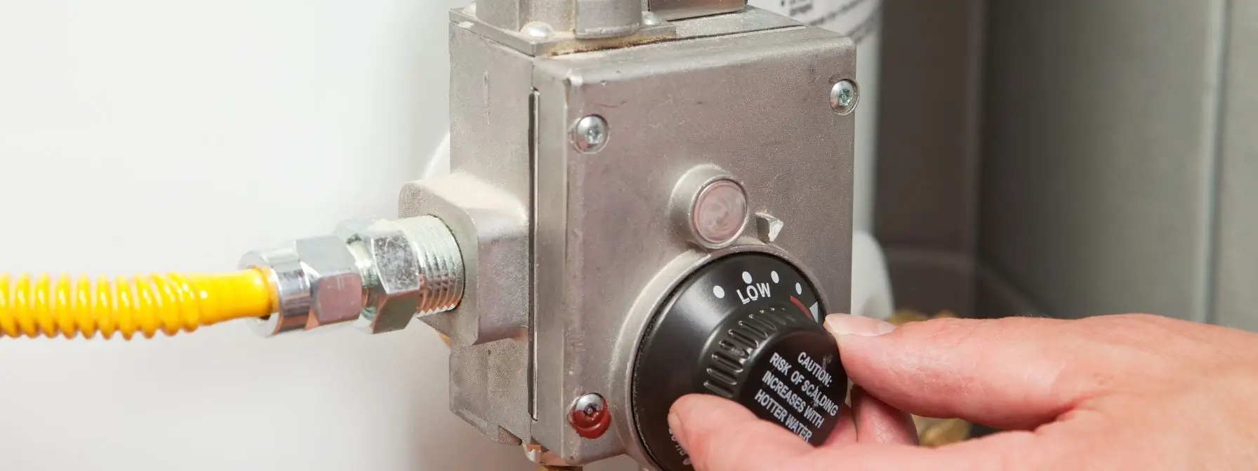 Close-up of a person's hand adjusting the temperature dial on a home water heater, highlighting the importance of proper maintenance to prevent plumbing issues and energy waste. Close-up of a person's hand adjusting the temperature dial on a home water heater, highlighting the importance of proper maintenance to prevent plumbing issues and energy waste.