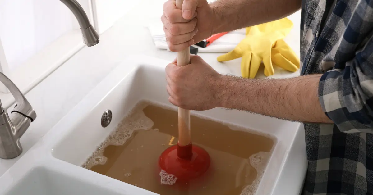 A person uses a plunger to clear a clogged kitchen sink filled with dirty water A person uses a plunger to clear a clogged kitchen sink filled with dirty water