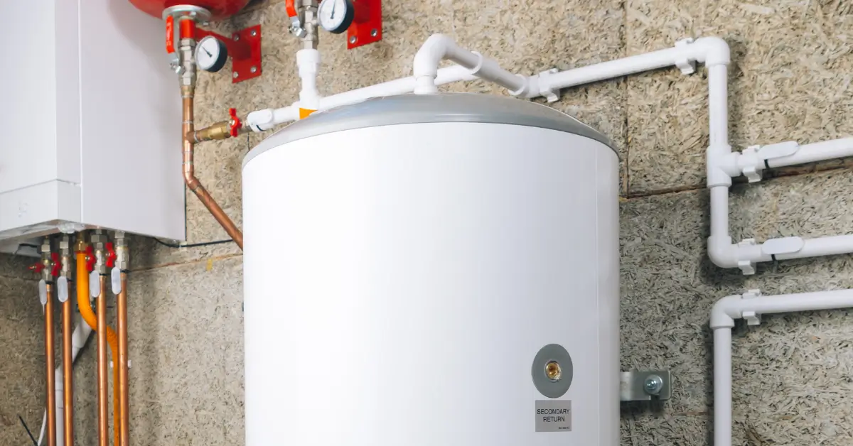 A large white storage water heater is installed in a utility room, connected to multiple copper and plastic pipes with gauges and valves visible on the surrounding plumbing system. A large white storage water heater is installed in a utility room, connected to multiple copper and plastic pipes with gauges and valves visible on the surrounding plumbing system.