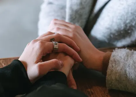 Couple holding hands with a small heart tattoo on one finger (anonymized case study image)