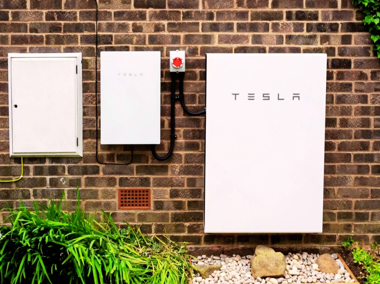 Tesla Powerwall mounted on a red brick wall in the UK.