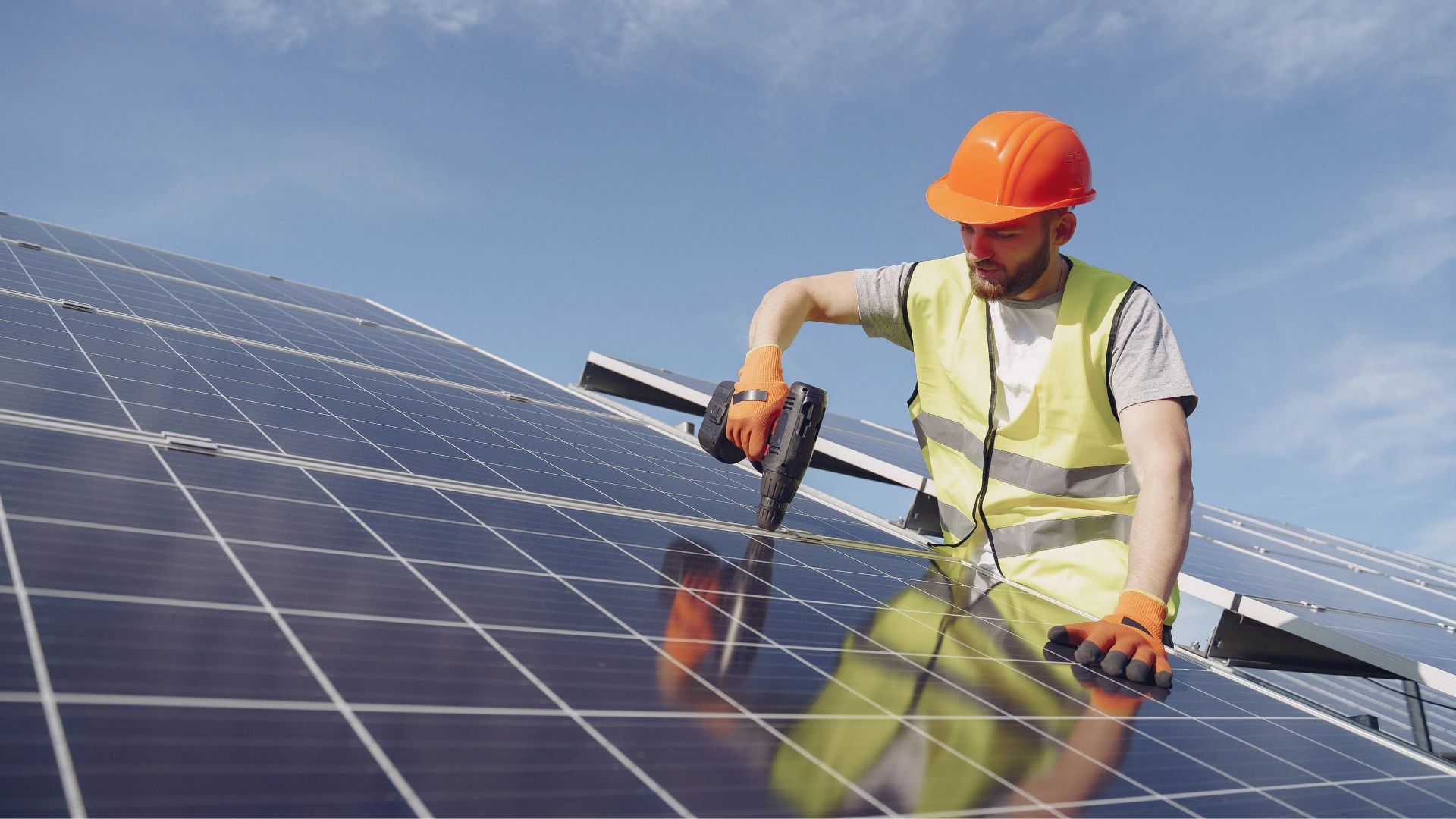 A solar installer wearing protective equipment installing a grand mounted solar panel.