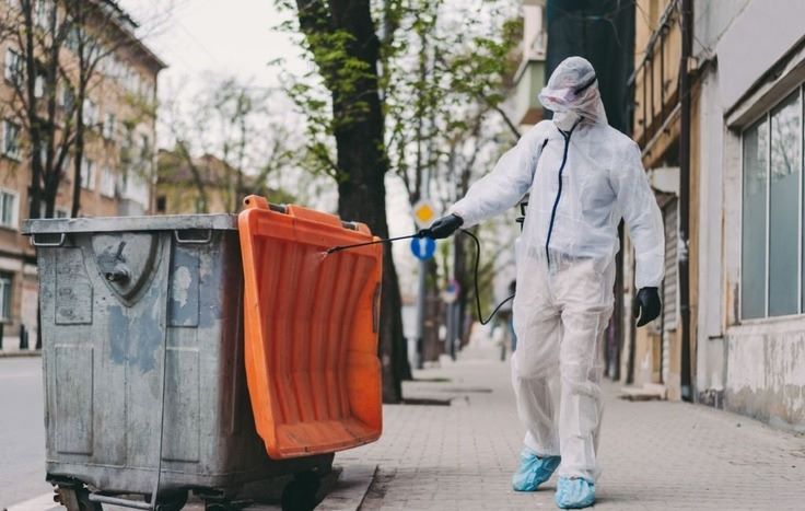 a guy spraying disinfectant on dumpster