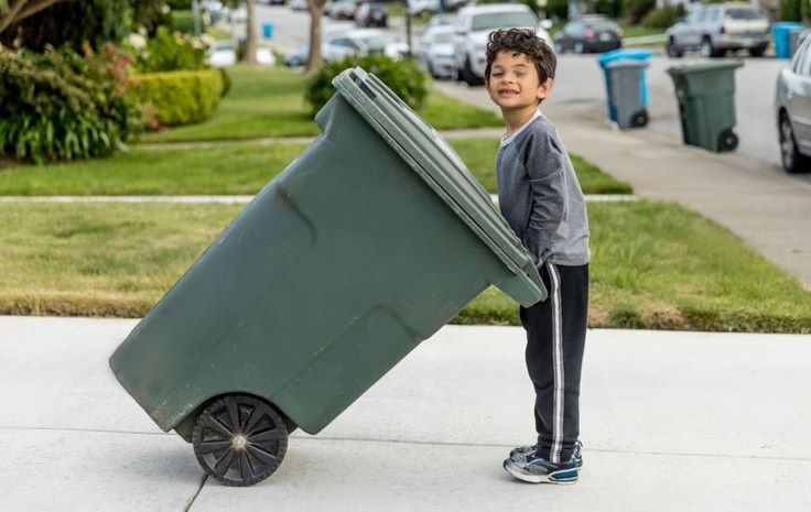 a kid pulling a garbage can with wheels