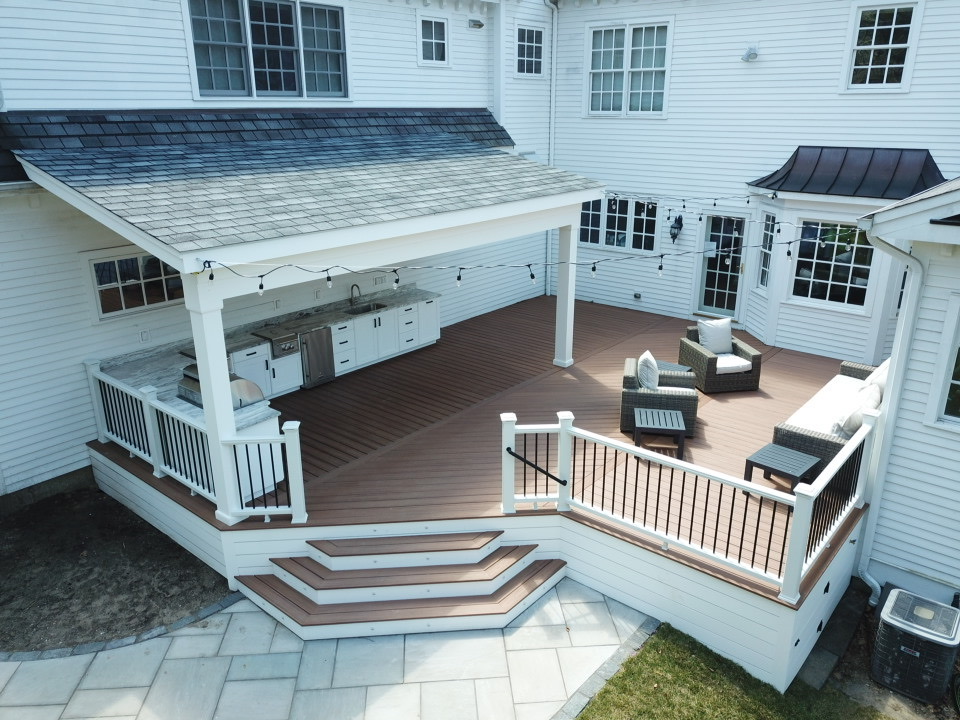 Covered deck with white posts, an outdoor kitchen and wicker seating on brown composite boards | Prime Decks Delaware, serving Hockessin, DE